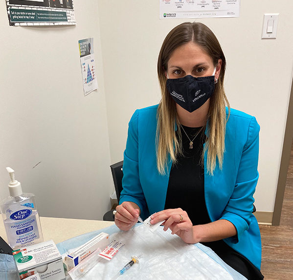 Dr. Mia Bondi, a primary care nurse practitioner in the community and researcher at UHN’s Toronto Centre for Liver Disease sitting at a table with a mask on.