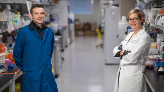 Dr. Mark Reed (L) and Dr. Valerie Wallace (R) smiling for the photo standing in the lab in lab coats.