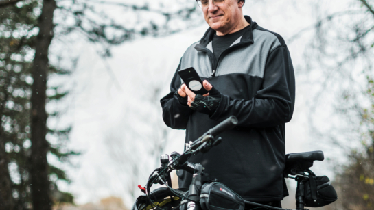 Patient Brad Pope outdoors standing next to a bicycle, he is holding an iPhone and smiling at it as he checks it.