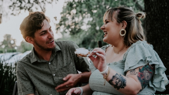 Two people sitting outdoors eating food, they look like they are in conversation and are laughing.