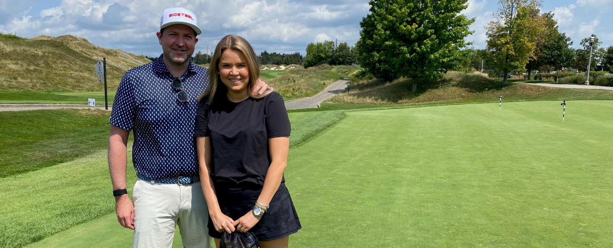 Alley Adams and Craig Mode posing for a photo on a golf course with a road in the background.