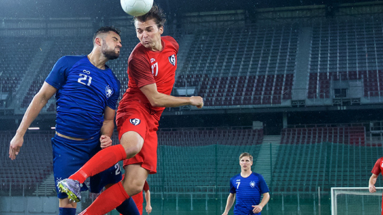 A group of people play soccer on a professional soccer field while wearing blue uniforms and red uniforms