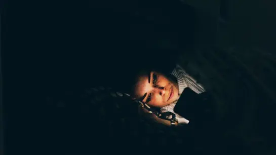 A person laying in bed in a dark room while on their phone with a bright light.