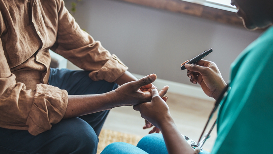 A health care worker holding the hand of a patient while examining them.