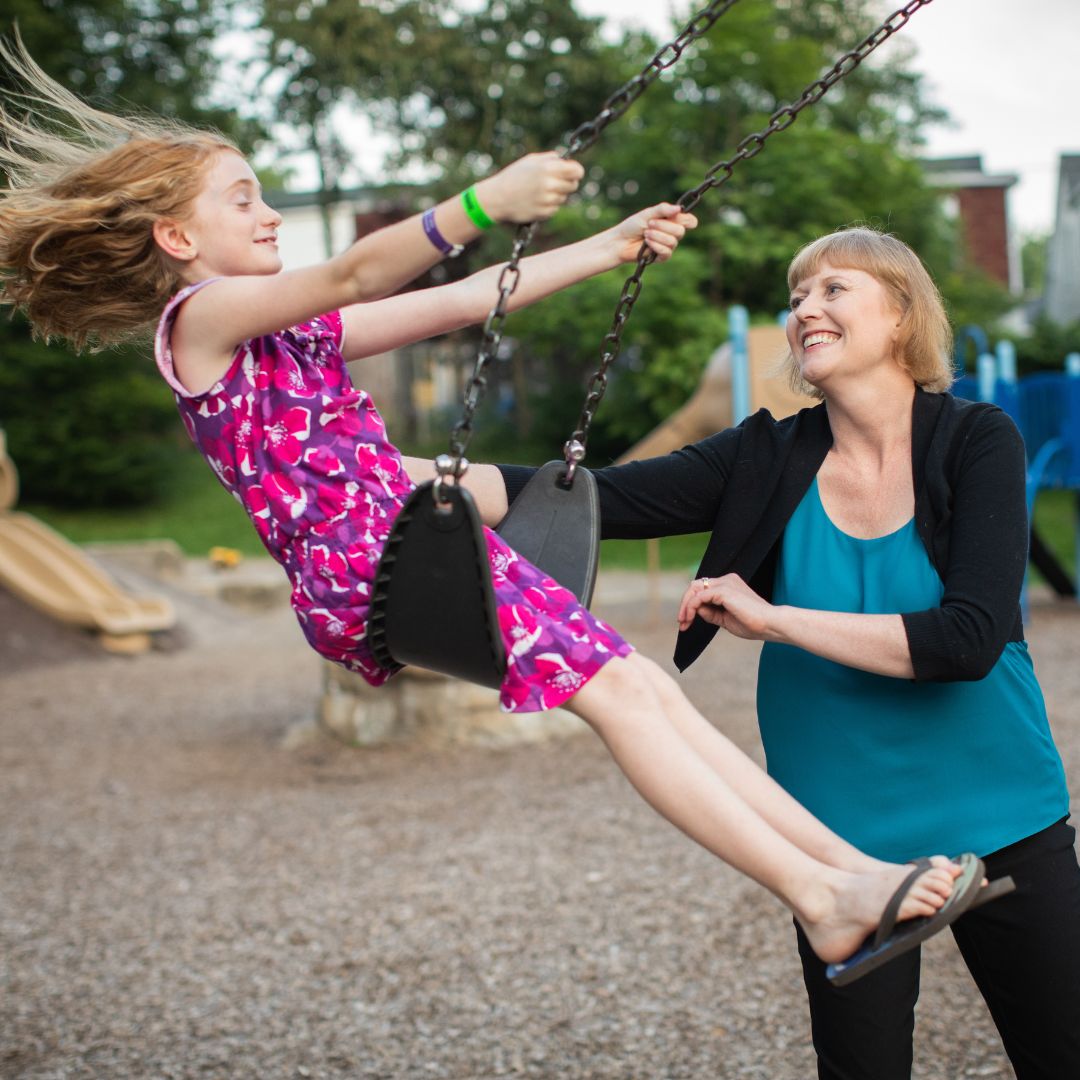 A mother pushing a daughter on a swing