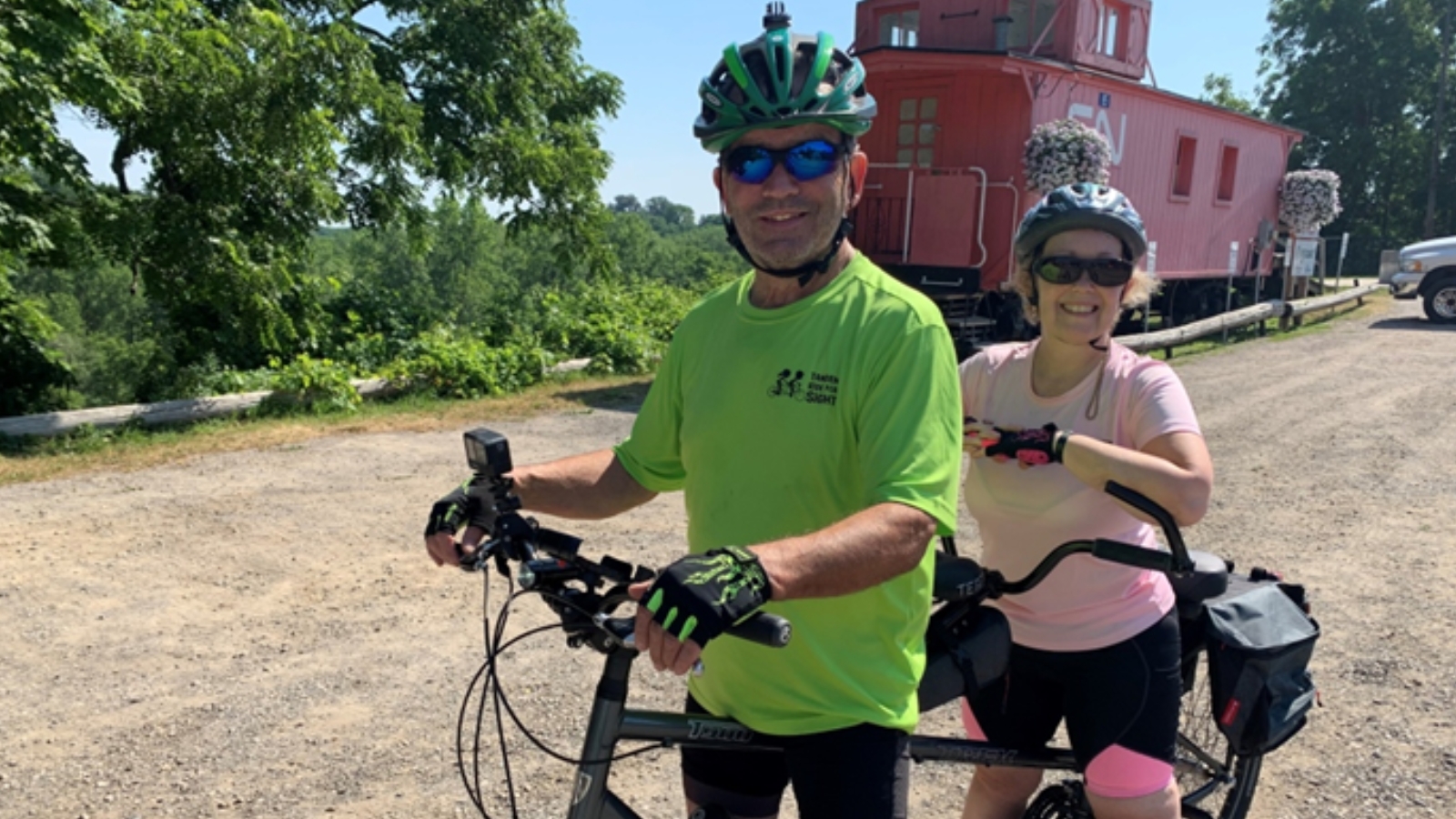 Amber Needham and her friend on a tandem bike with a train in the background on a warm sunny summer day.