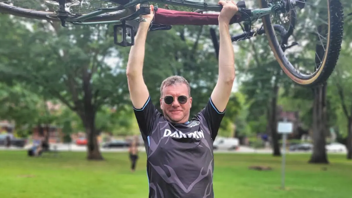 John holding his bike over his head at a park