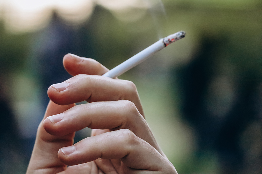 A hand holding a cigarette with smoke coming off of it