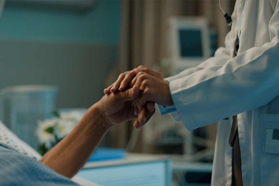 A stock image of a hospital bedside with a patient and doctor holding hands
