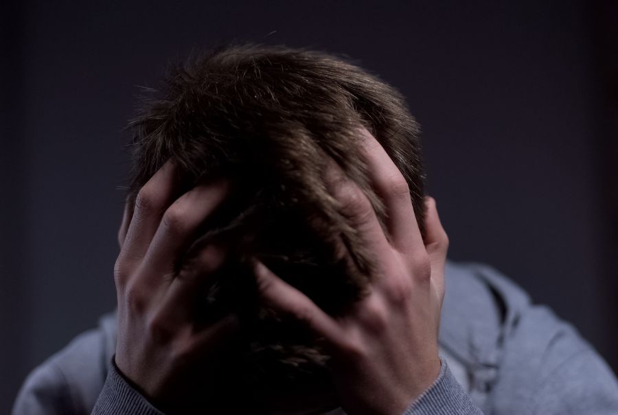 A person grabs their head with a dark background.